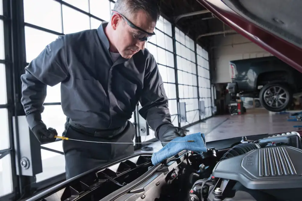 Technician wearing gloves checking the oil dipstick on a GMC vehicle's engine with the hood open.