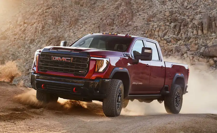 Dark red GMC Sierra HD truck kicking up dust on a rocky desert trail.
