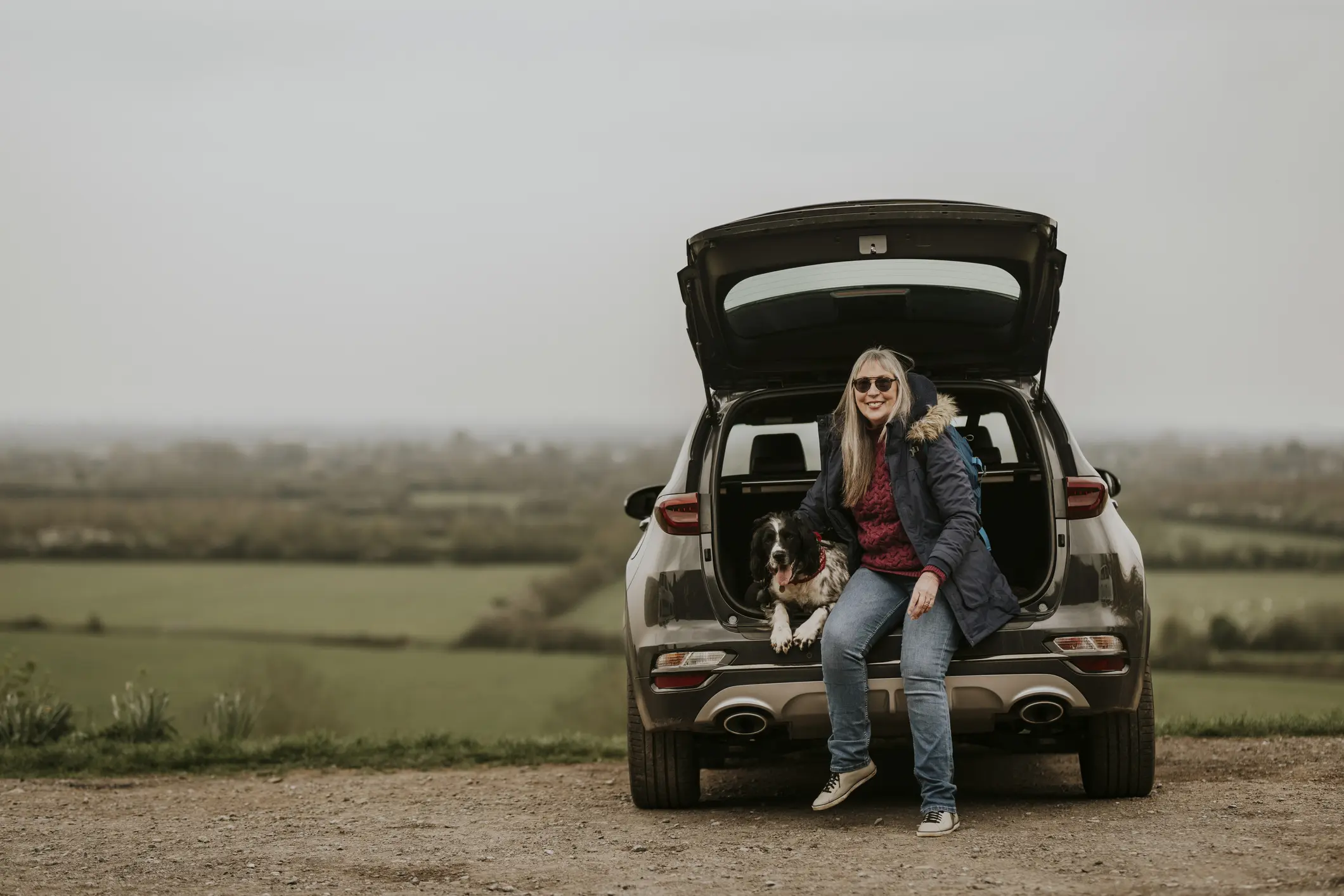Lady with dog sitting in the back of a suv