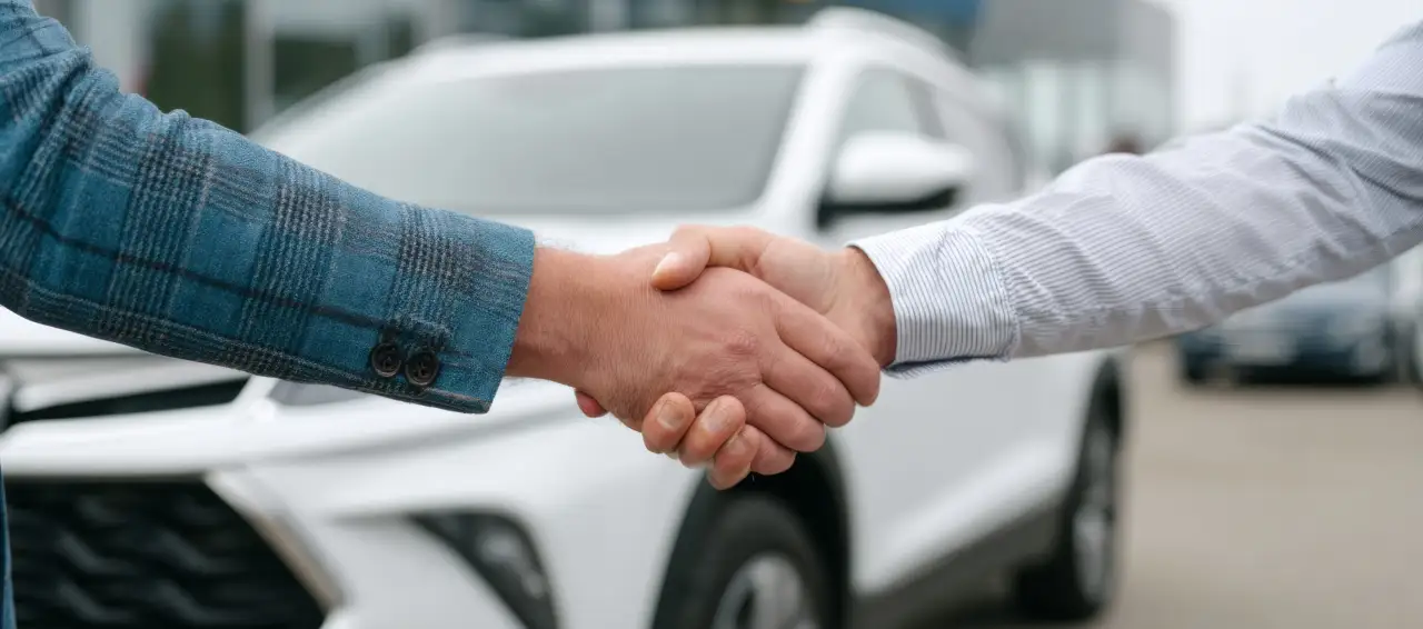 Salesperson and customer shaking hands in front of a white SUV at the dealership