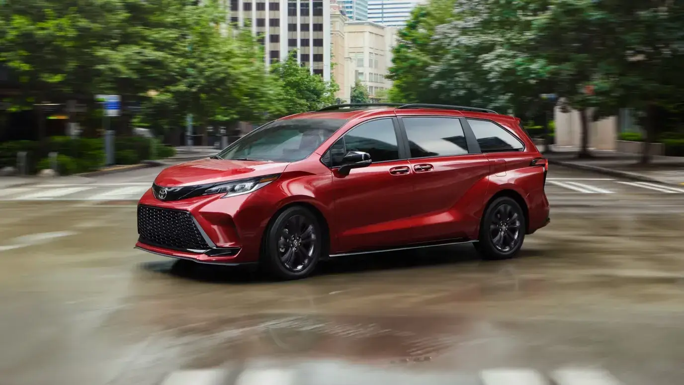 Red 2026 Toyota Sienna driving through a city intersection, front three-quarter view