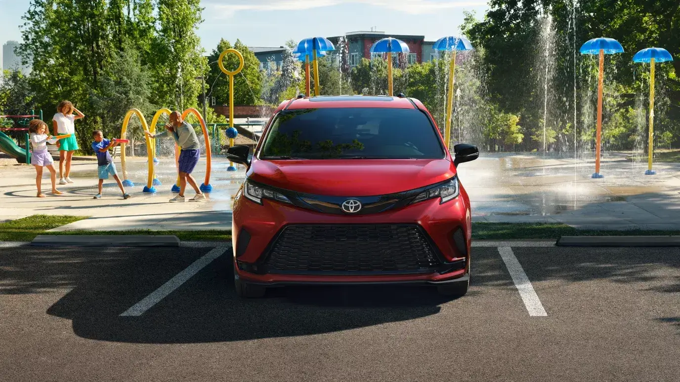 Red 2026 Toyota Sienna parked by a splash-pad playground, front view