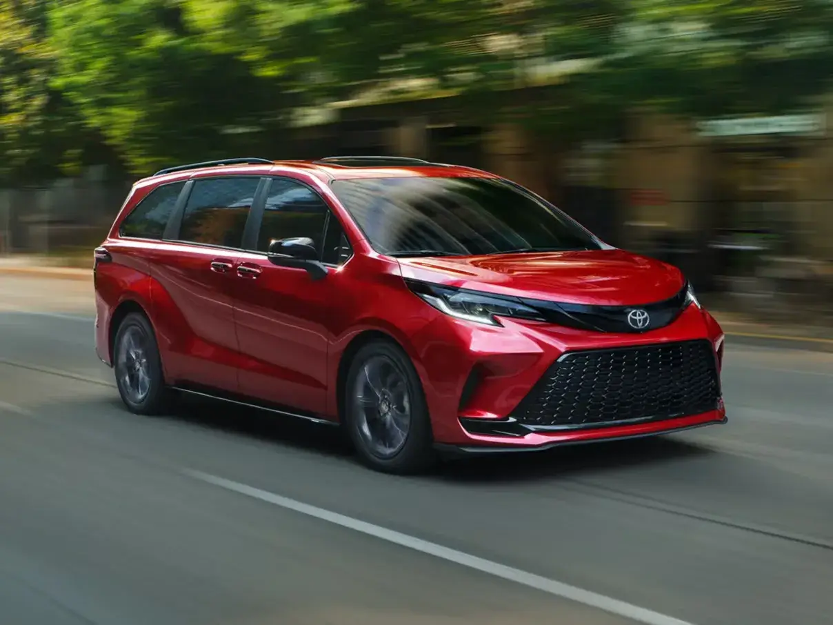 Red 2026 Toyota Sienna driving on a tree-lined road, front three-quarter view