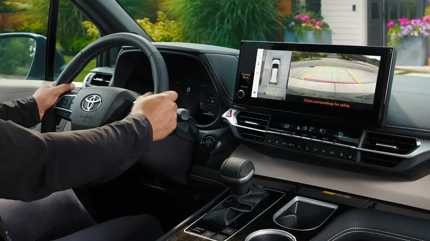 Driver at the wheel of a 2026 Toyota Sienna, touchscreen showing the camera view
