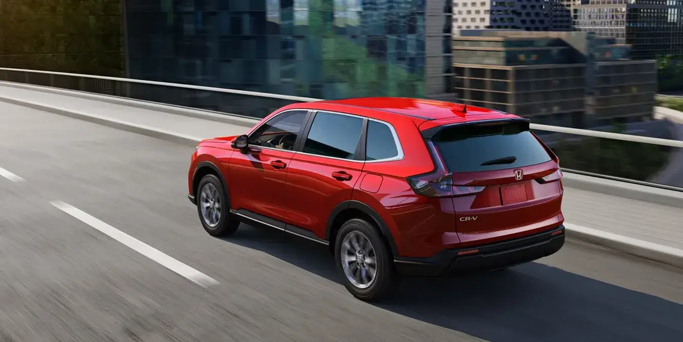 Red 2027 Honda CR-V driving on a city highway, rear three-quarter view