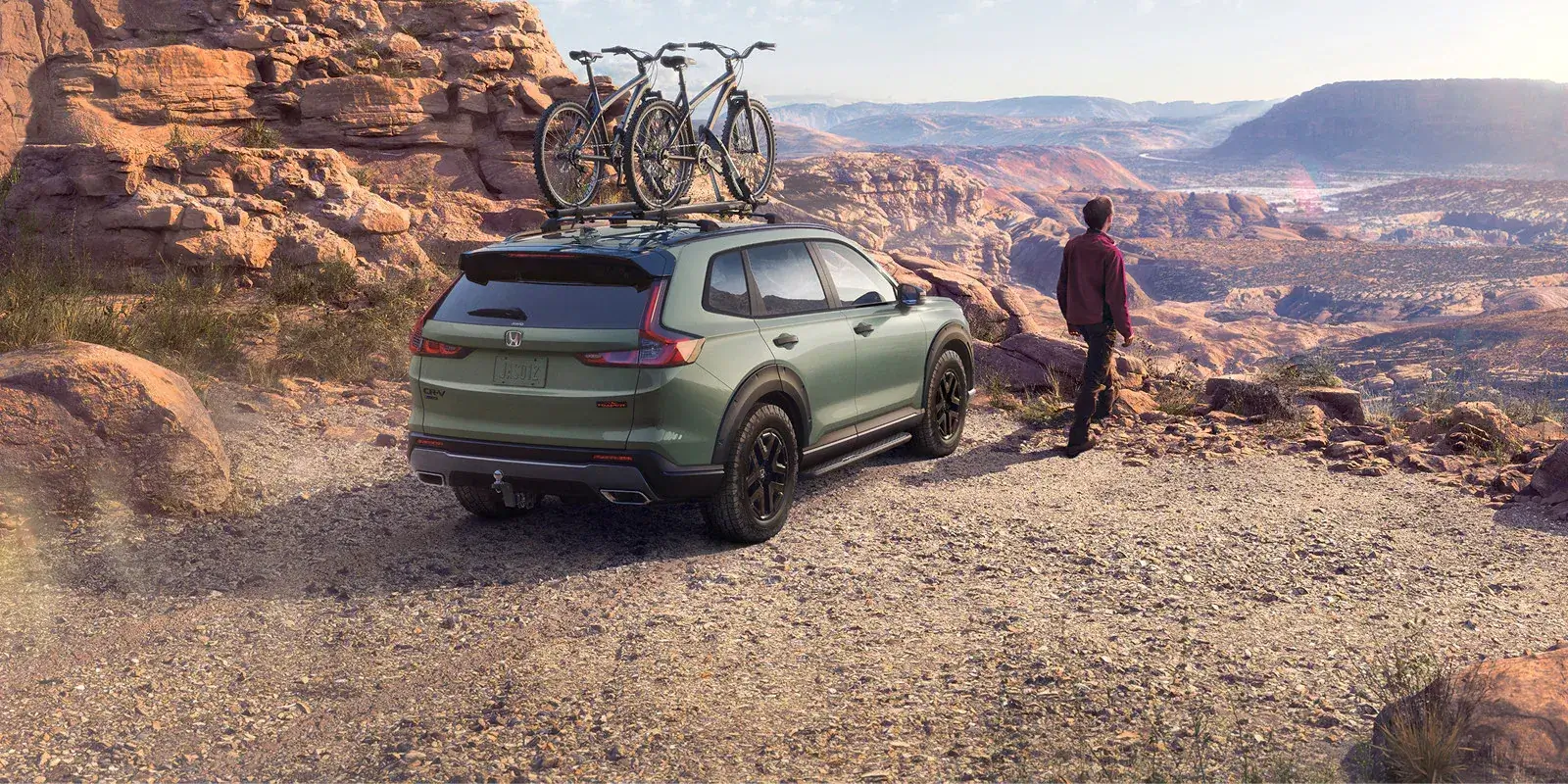 Green 2027 Honda CR-V with roof-rack bikes, rear three-quarter view at a canyon overlook