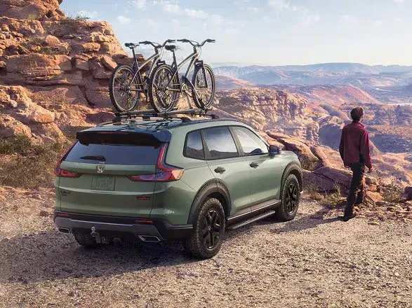 Green 2027 Honda CR-V with roof-rack bikes, rear three-quarter view at a canyon overlook