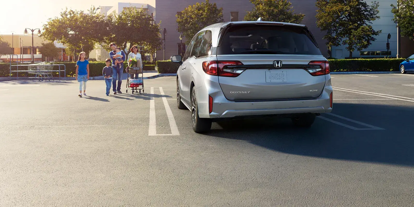 Silver 2027 Honda Odyssey parked in a lot as a family walks over, rear view