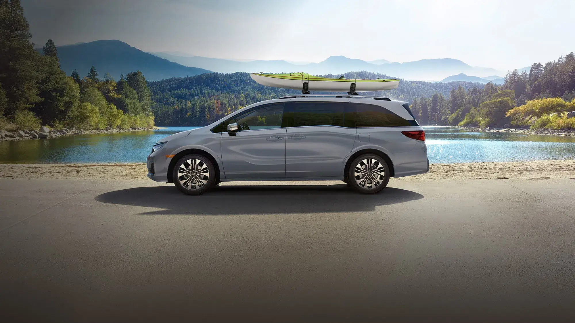 Silver 2027 Honda Odyssey with kayaks on the roof parked by a mountain lake