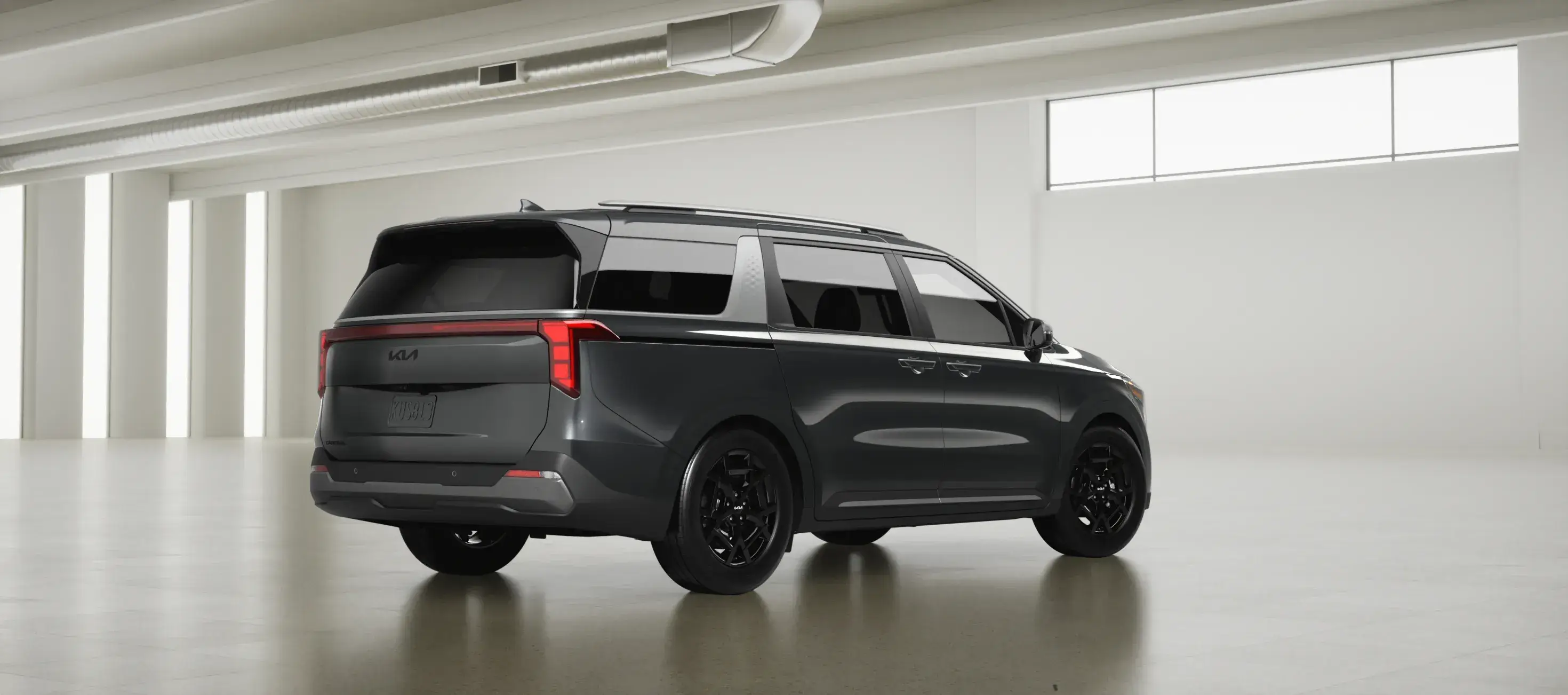Gray 2027 Kia Carnival in a white studio, rear three-quarter view facing right