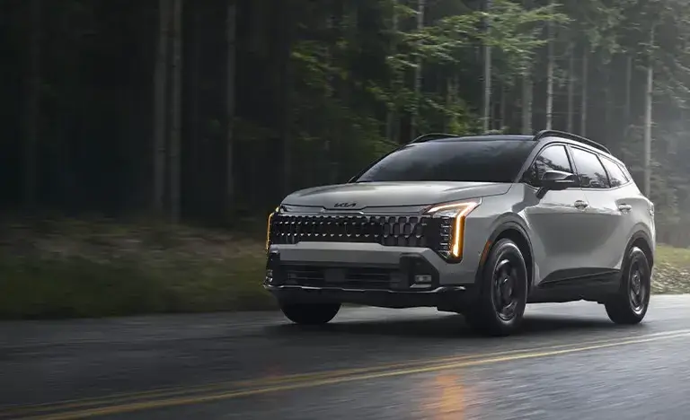 Gray 2027 Kia Sportage driving on a rainy forest road, front three-quarter view
