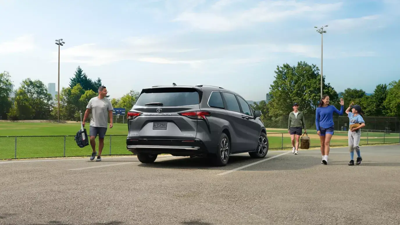 Gray 2026 Toyota Sienna parked by a ballfield as a family unloads, rear three-quarter view