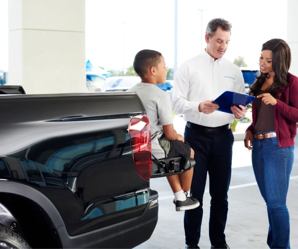 Honda representative reviewing information with a customer and child beside a Honda pickup truck