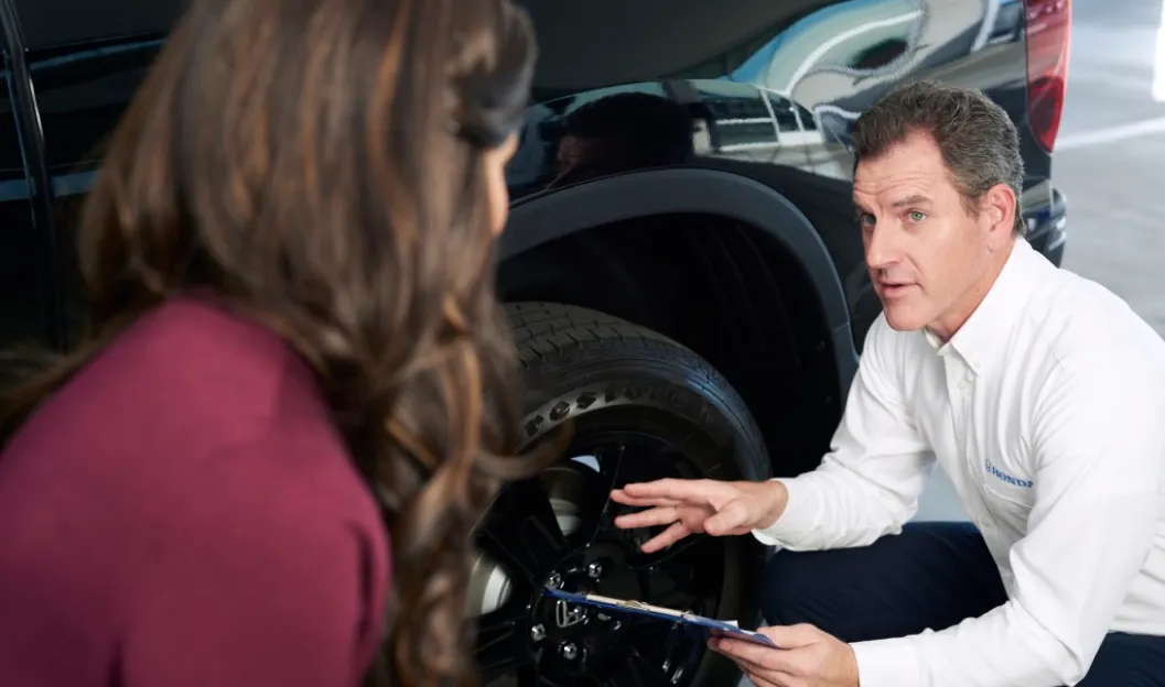 Honda service advisor explaining vehicle service details to a customer beside a Honda SUV wheel