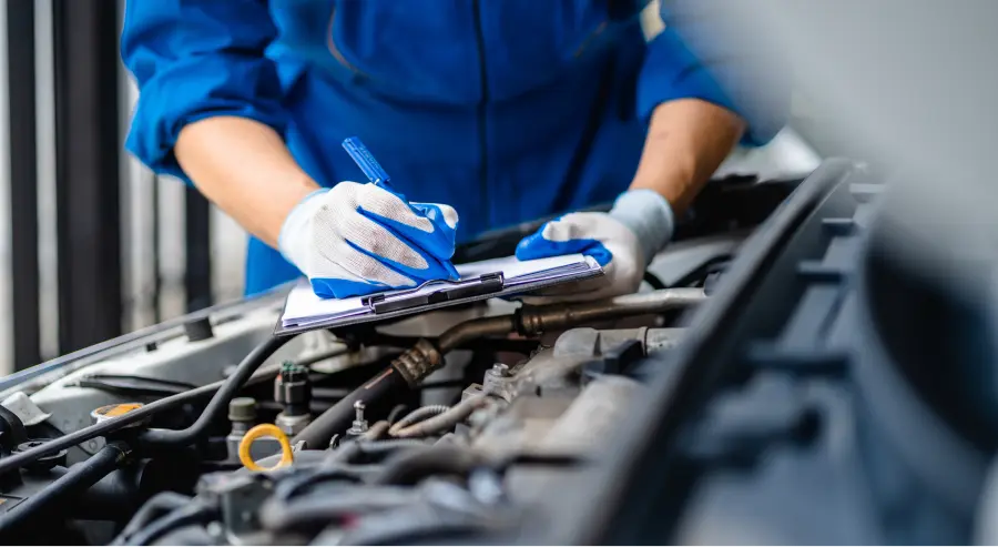 Mechanic taking notes on a clipboard while inspecting a vehicle's engine bay