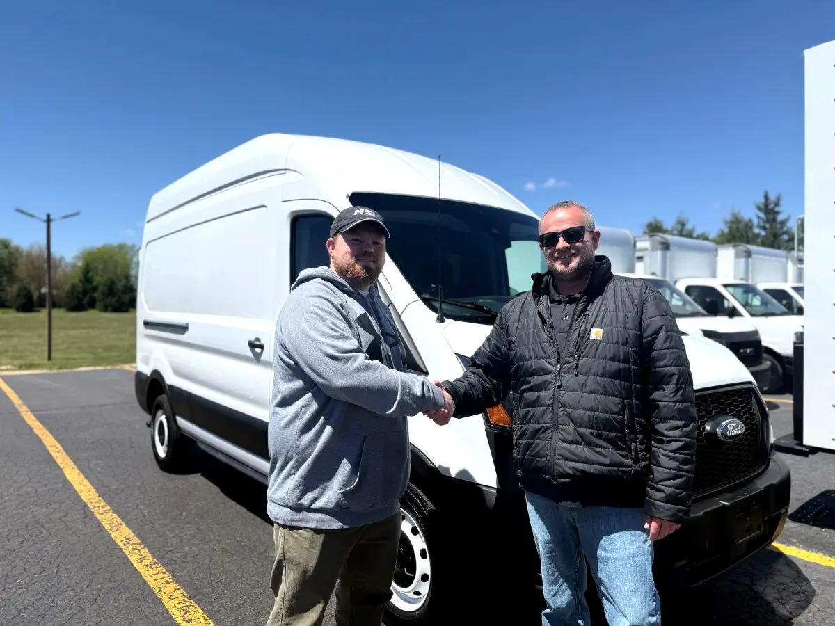 Trebor Verwey of Midwest Solutions Inc. shaking hands with Sales Manager Chris Roberts at Signature Truck after taking delivery of a Ford Transit high-roof cargo van in Crystal Lake Illinois