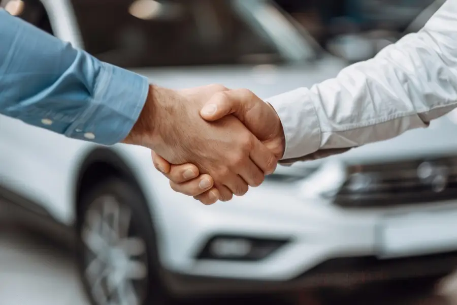 Two people shaking hands in front of a white SUV at a car dealership