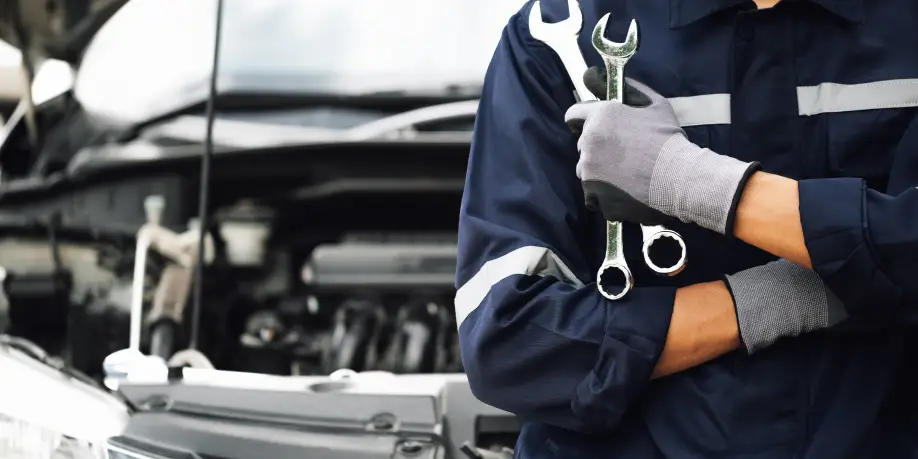 Service technician holding wrenches beside a car with the hood open