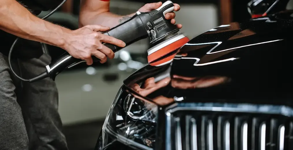 Technician polishing the exterior of a luxury vehicle during detailing service