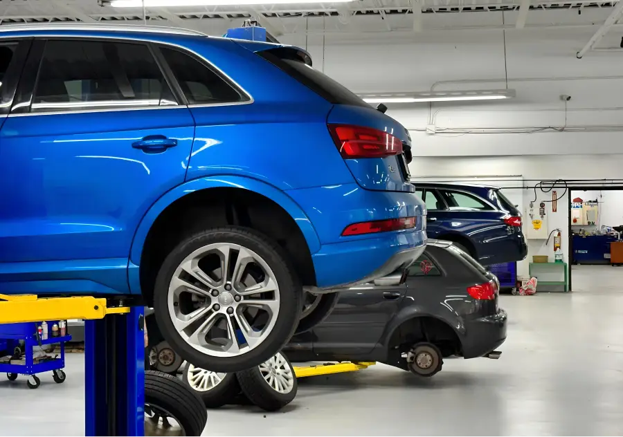 Blue SUV elevated on a lift in an auto repair shop with other vehicles being serviced in the background