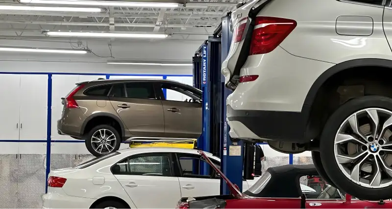 Blue SUV raised on a lift in a repair shop with another vehicle being serviced below