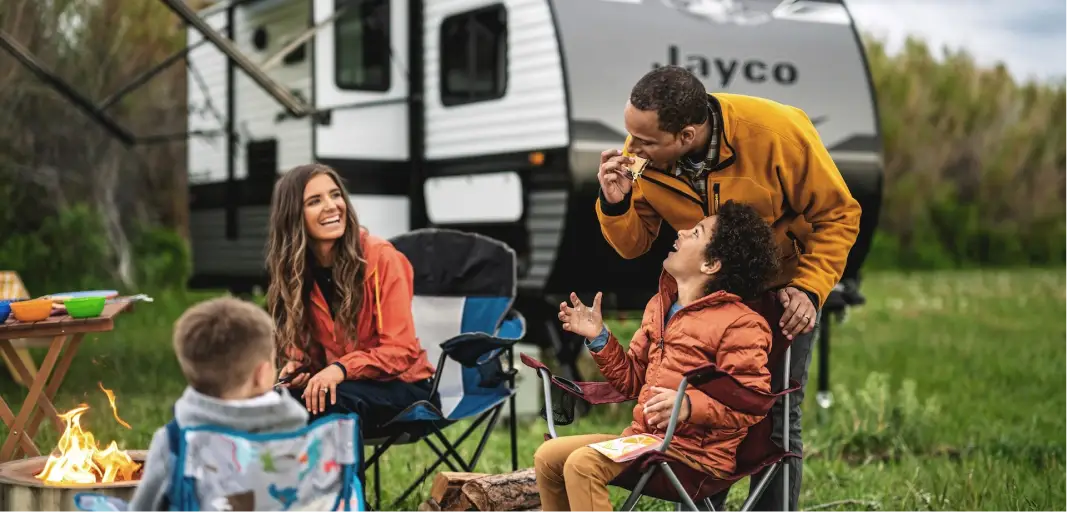 Family sitting around a campfire in front of a travel trailer RV.
