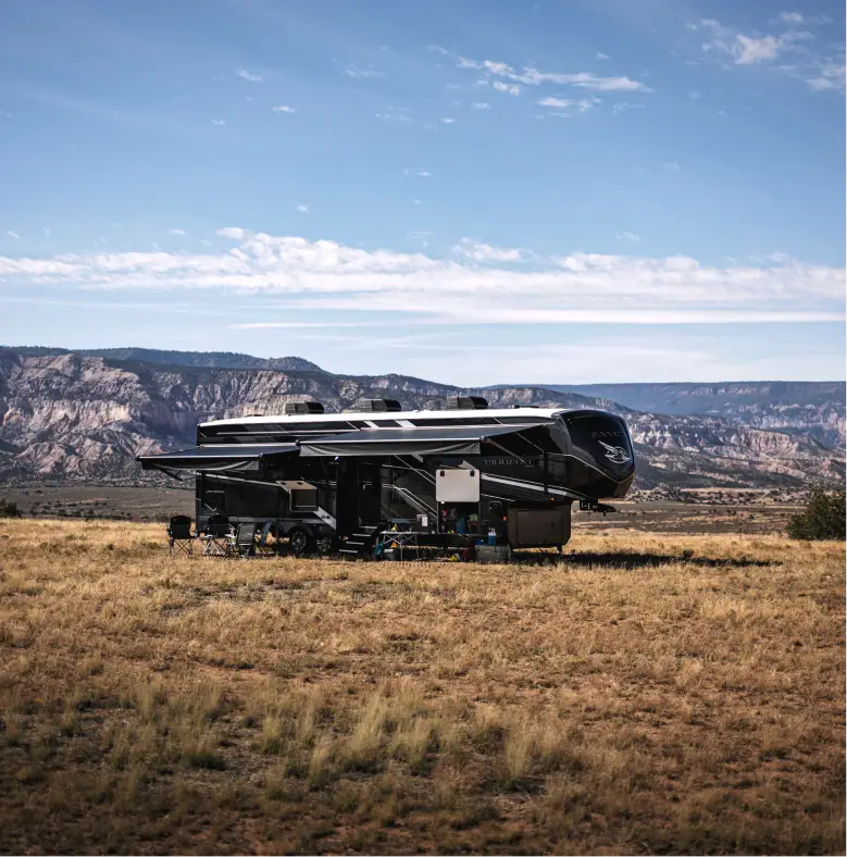 Fifth wheel RV parked in an open landscape with mountains in the background.