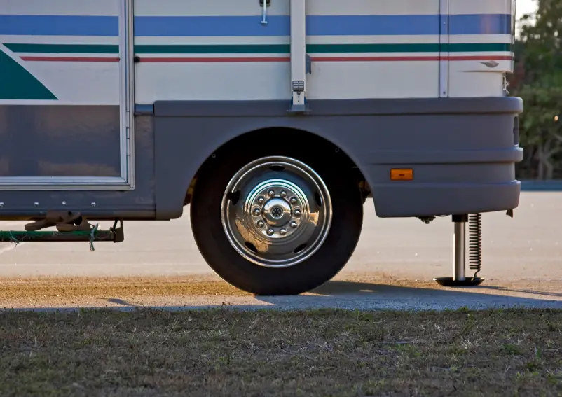Close-up of an RV wheel and stabilizer jack on a parked vehicle.