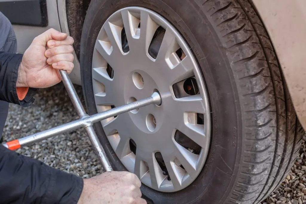 Hands disassembling a modern car wheel (steel rim) with a lug wrench