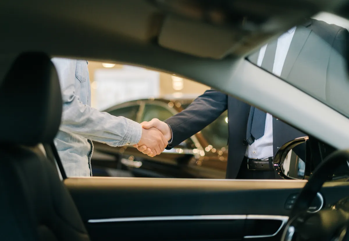 Customer shaking hands with a dealership representative beside a vehicle