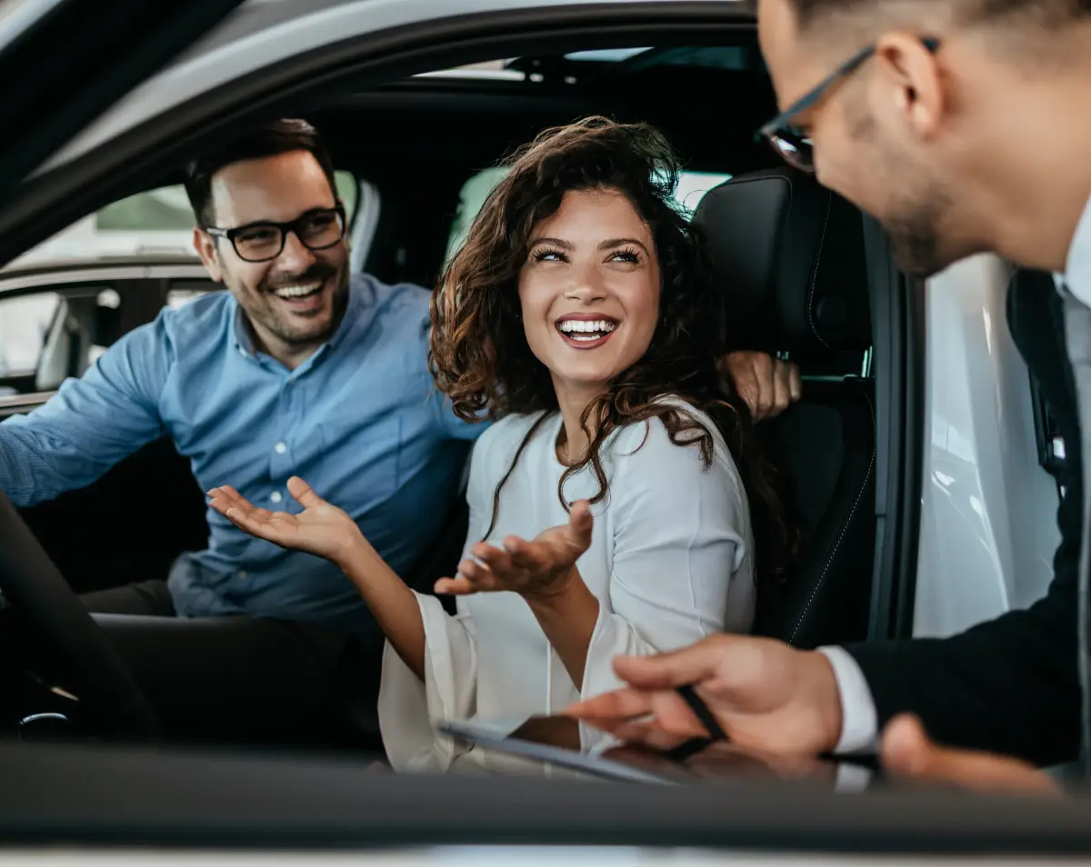 Couple speaking with a dealership representative inside a used vehicle