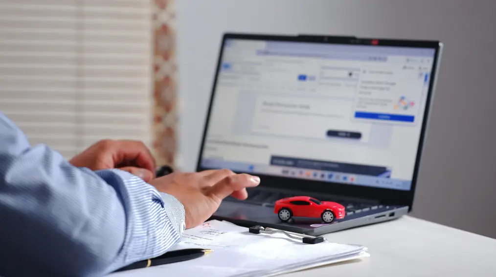 Customer researching a used vehicle online with a laptop and paperwork on a desk