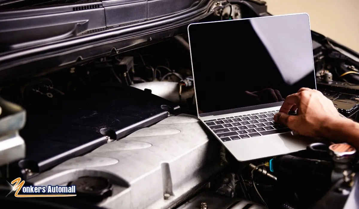 A certified automotive technician uses a laptop to run a diagnostic scan on a vehicle with the hood open at Yonkers Automall's service center, with engine components and service tools visible in the background.