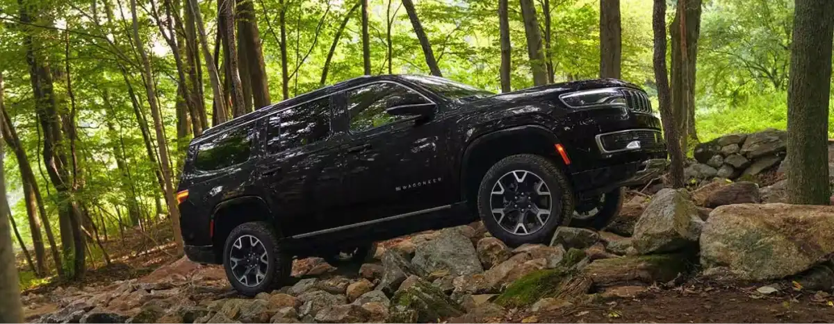 Black Jeep Wagoneer driving over rocks on a wooded off-road trail