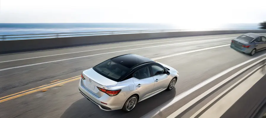 2025 Nissan Sentra in white taking a curve on a coastal highway